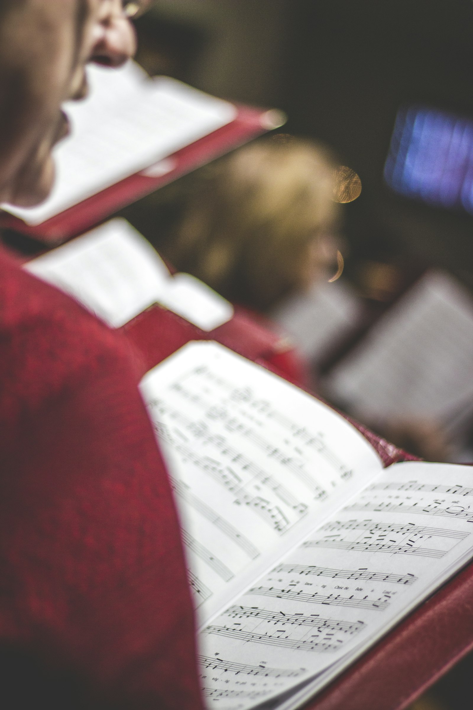 A robed singer holding an open music book in warm light