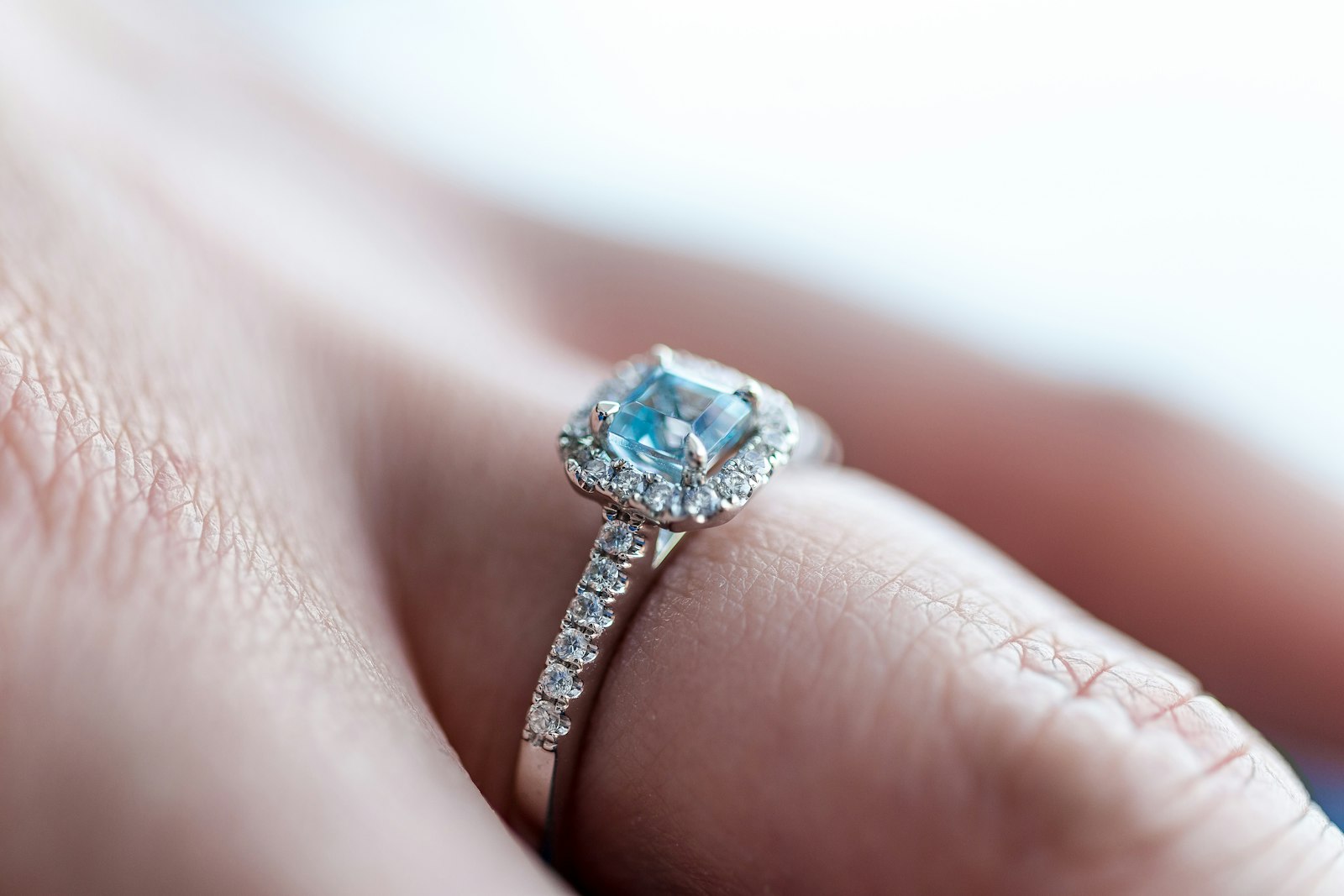An aquamarine halo ring on a finger, seen close up
