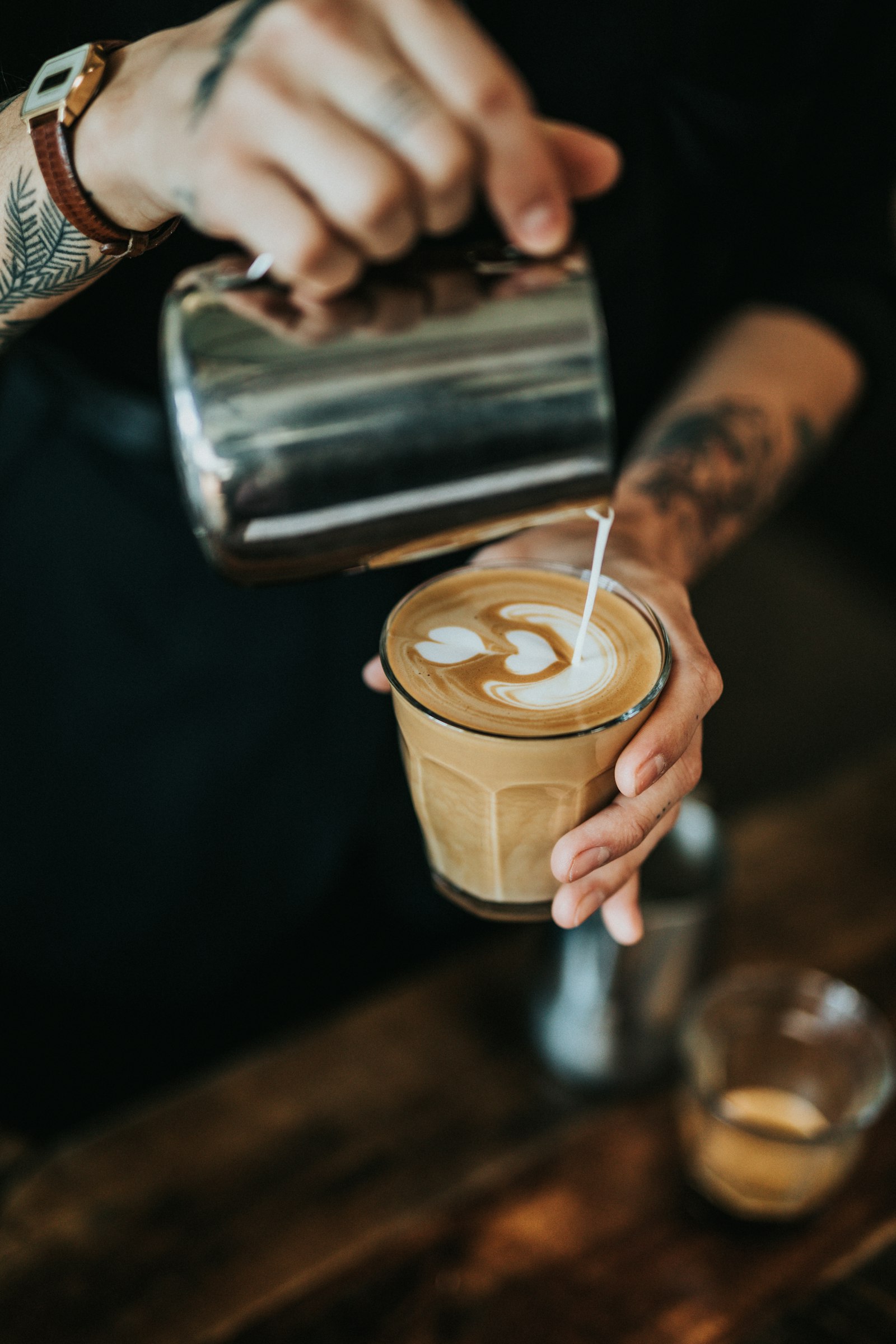 A barista pouring latte art into a glass