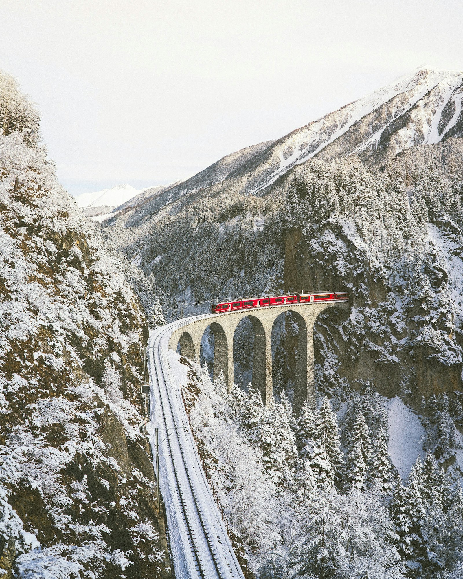 A red train crossing a stone viaduct in snowy forest