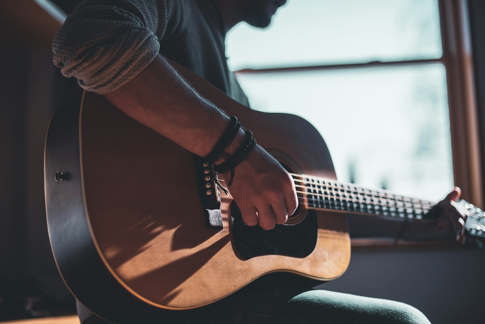A man playing an acoustic guitar by a window