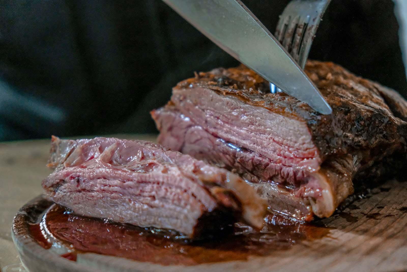 A knife slicing a medium-rare steak on a board