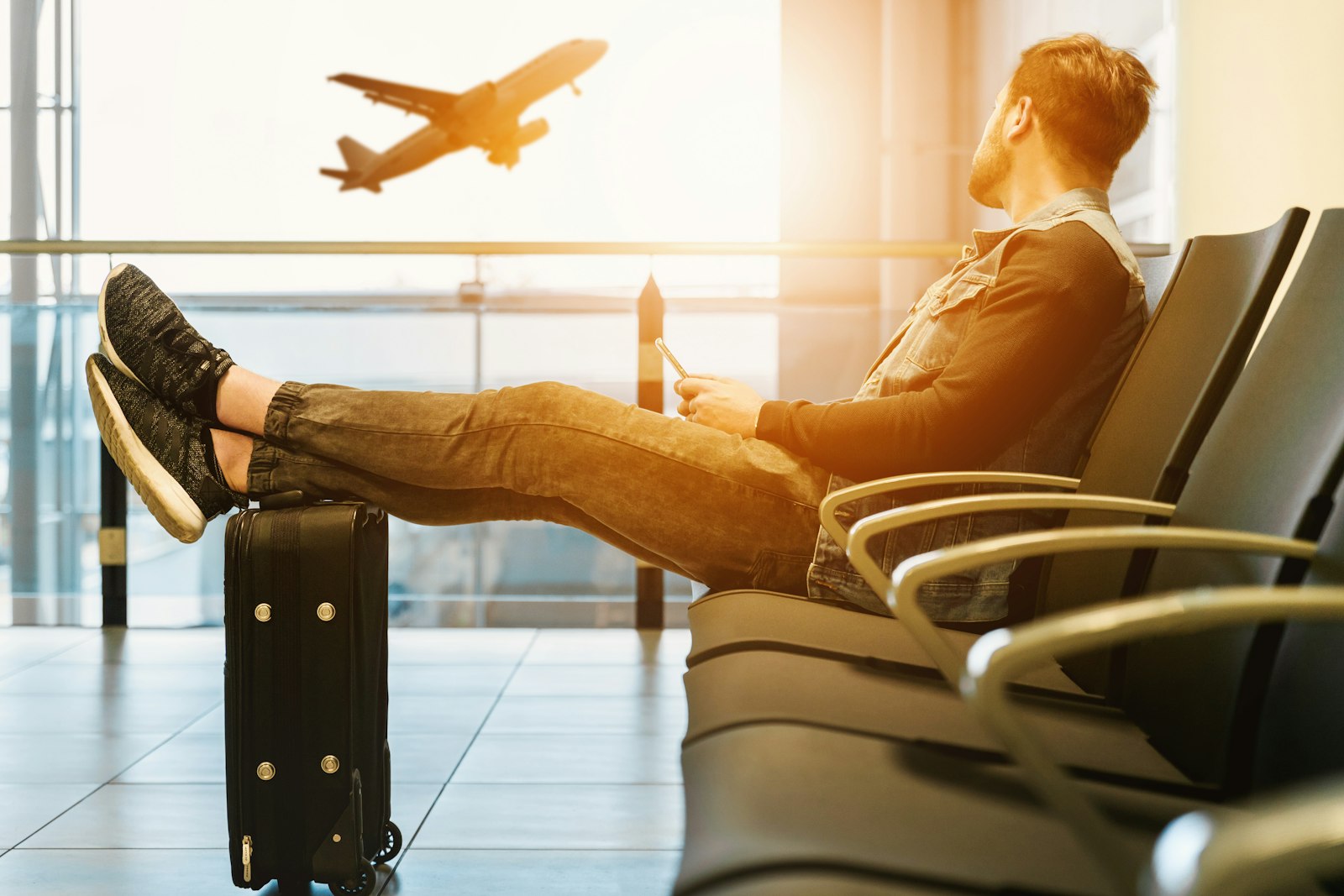 A traveller with his feet on a suitcase watching a plane take off