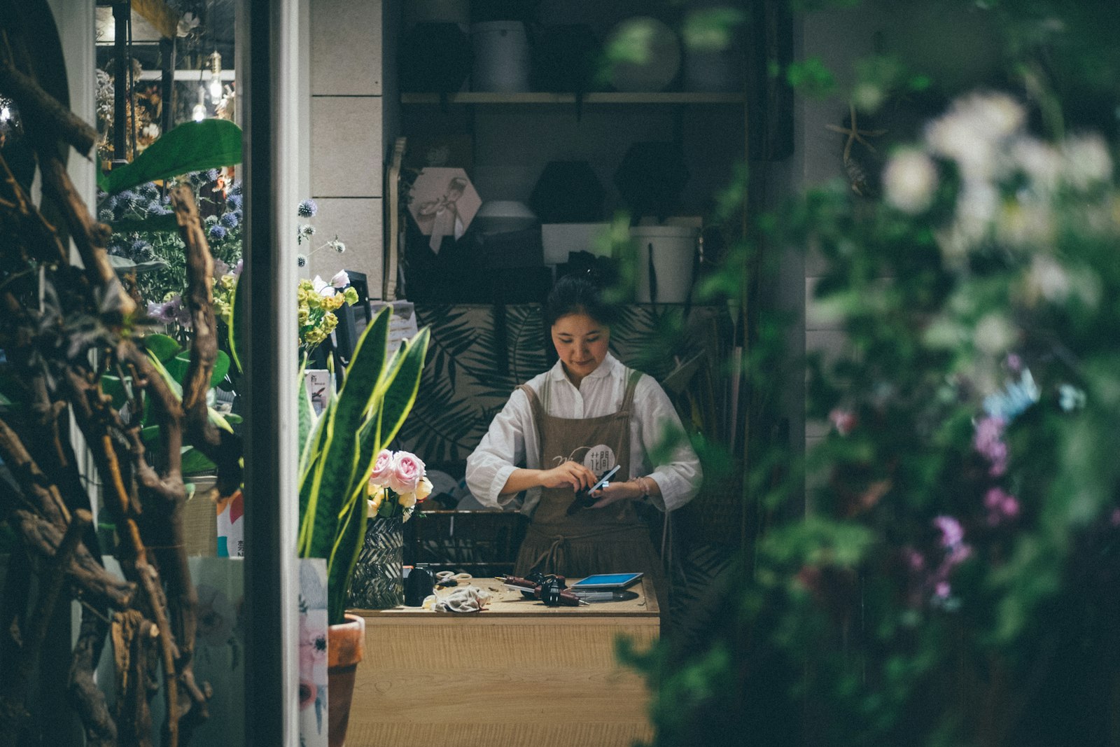 A florist in an apron working at her counter, seen through foliage