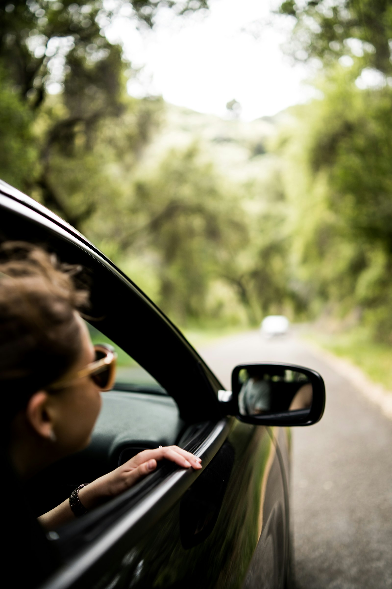 A young woman leaning out of a car window on a country road