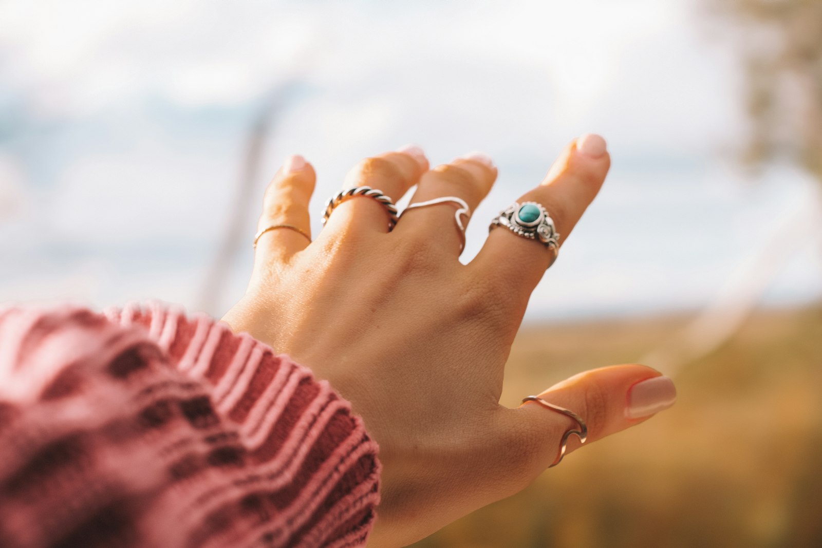 A hand wearing several silver rings against the sky