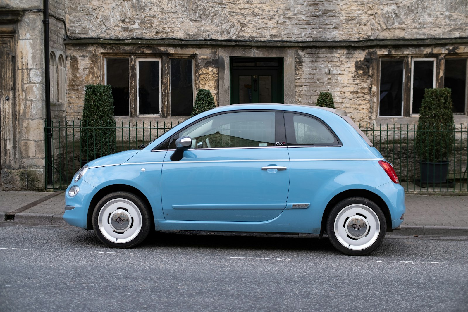 A small pale blue car parked in front of an old stone house