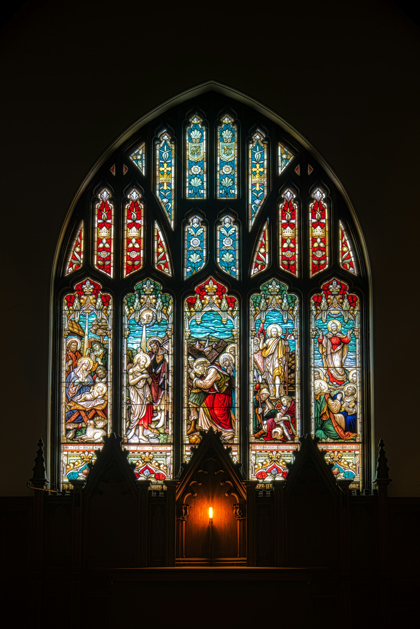 A gothic stained-glass window glowing above a candle