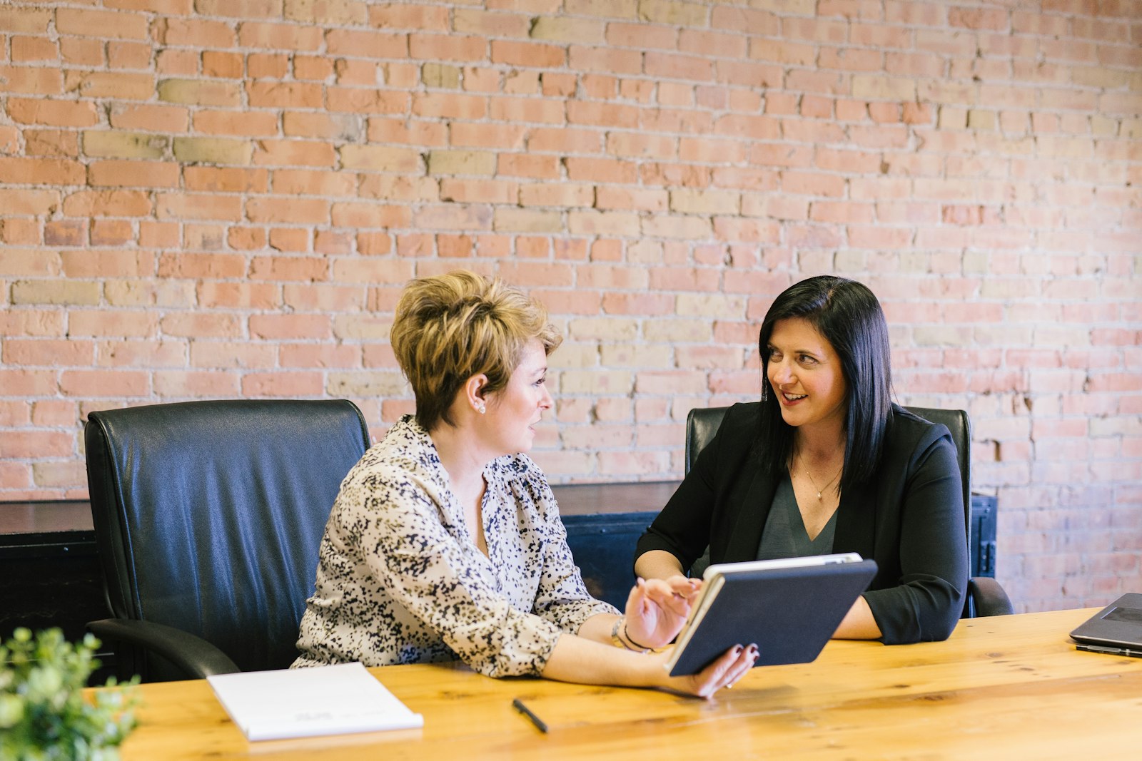 Two women talking in leather chairs at a table with a tablet