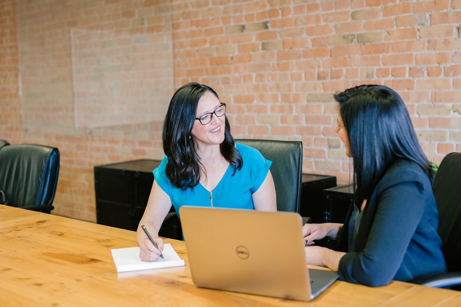 Two women talking across a desk in a brick-walled office