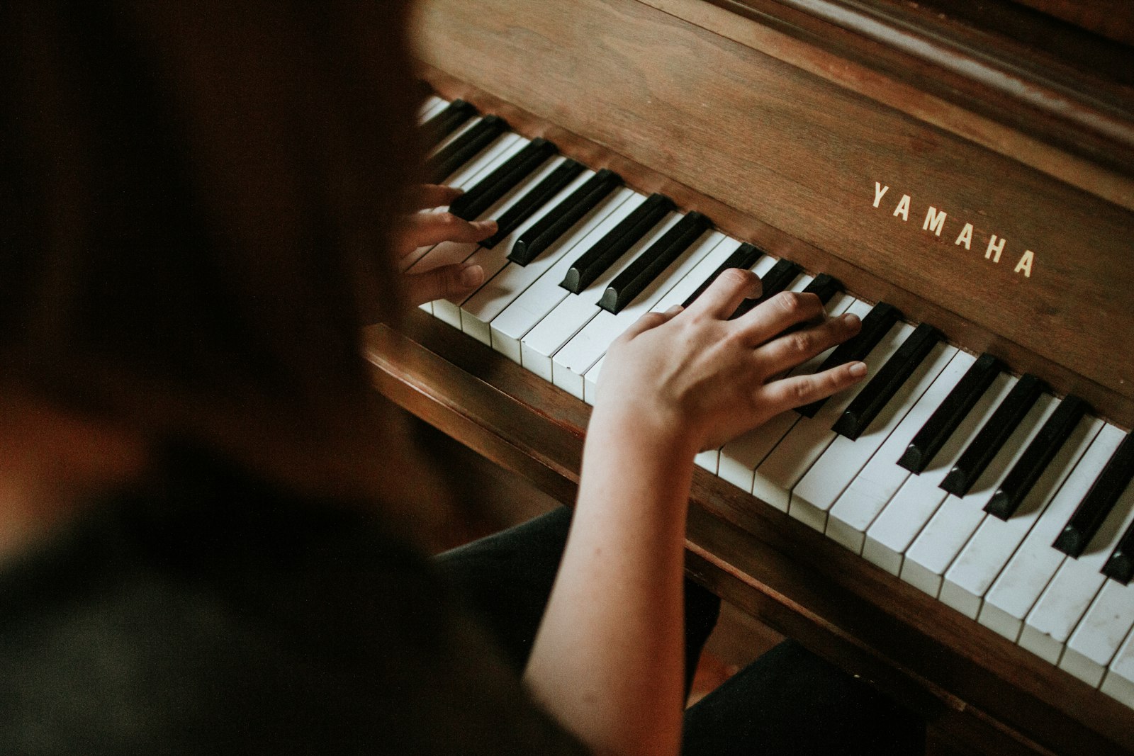 A woman playing an upright Yamaha piano in warm light