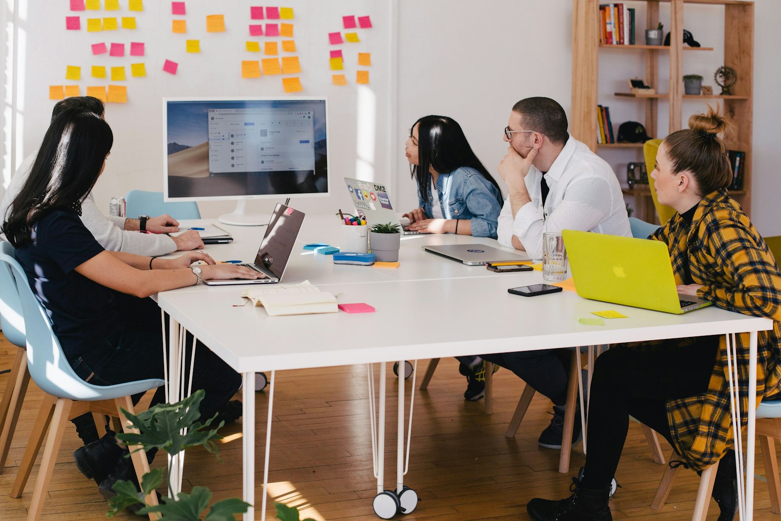 A team around a white table with laptops, sticky notes covering the wall behind them