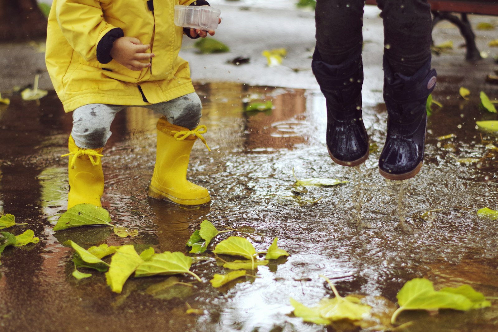 Toddlers in wellies splashing in a puddle