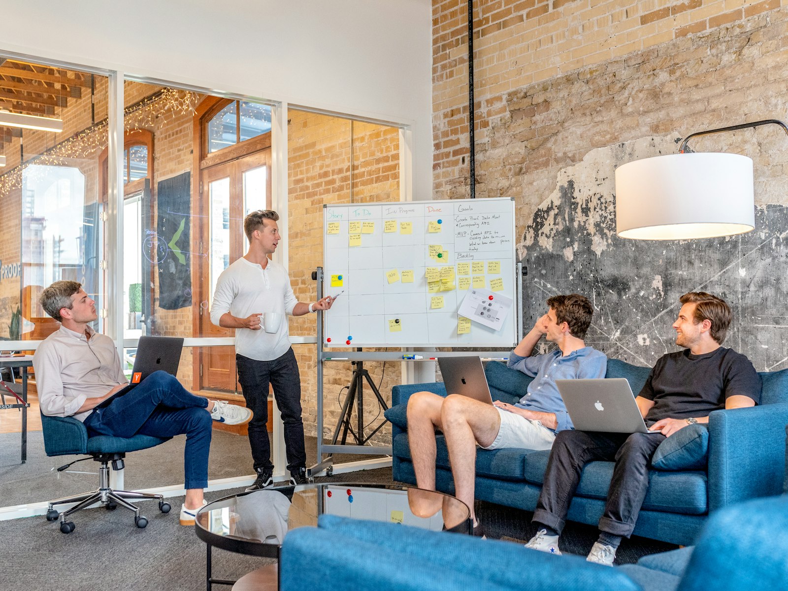 A man at a whiteboard covered in sticky notes leading a discussion with three colleagues