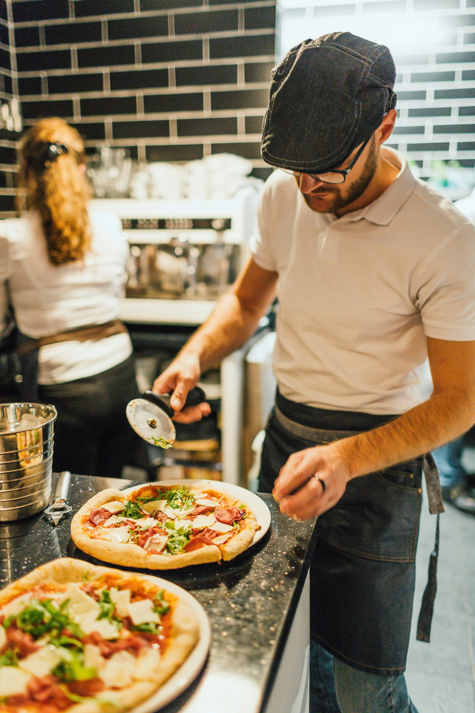 A pizzaiolo cutting pizzas at the counter