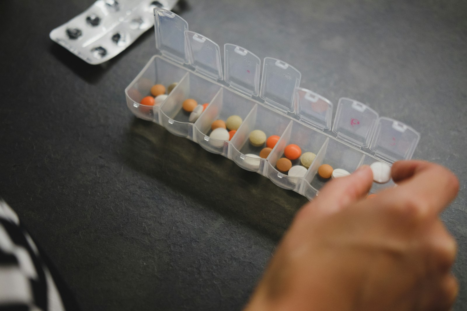 A hand filling a weekly pill organiser