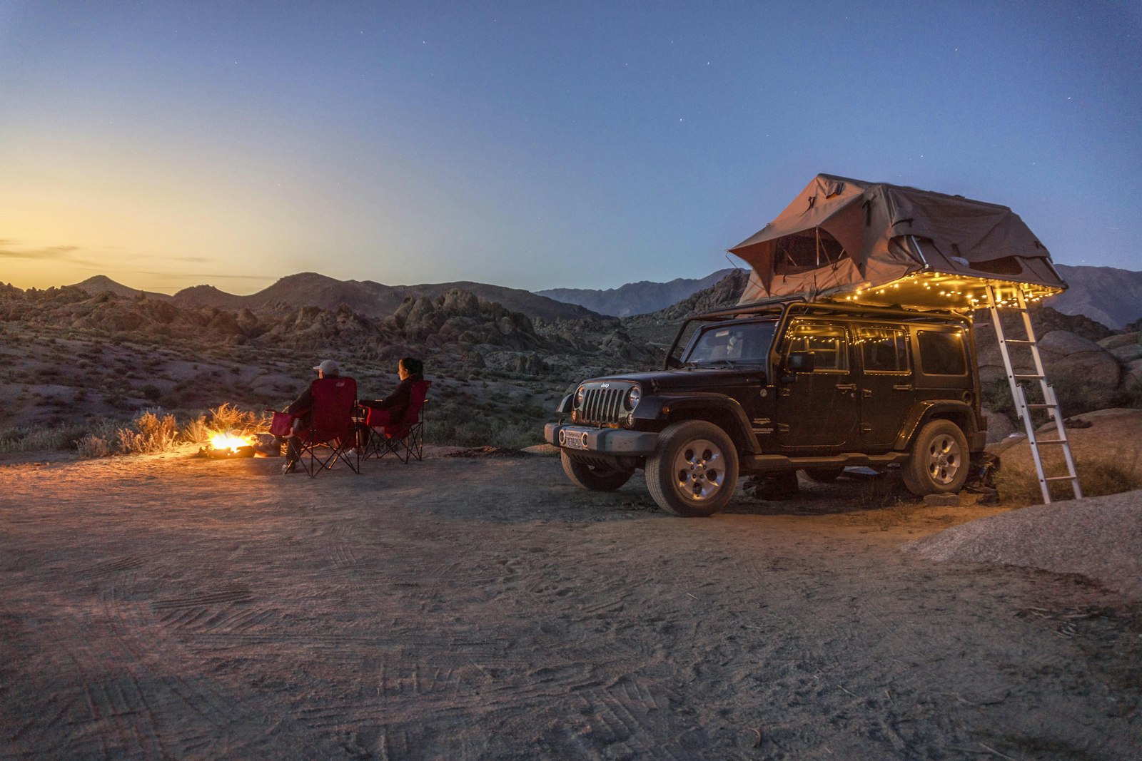 A 4x4 with an open rooftop tent and string lights by a campfire