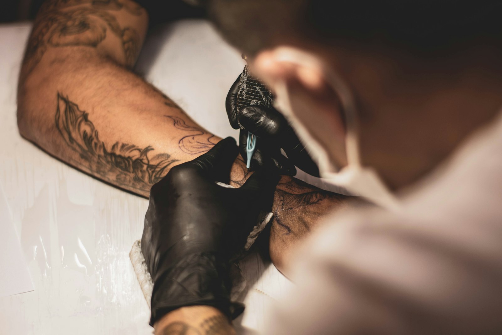 A masked artist shading an inked arm from above