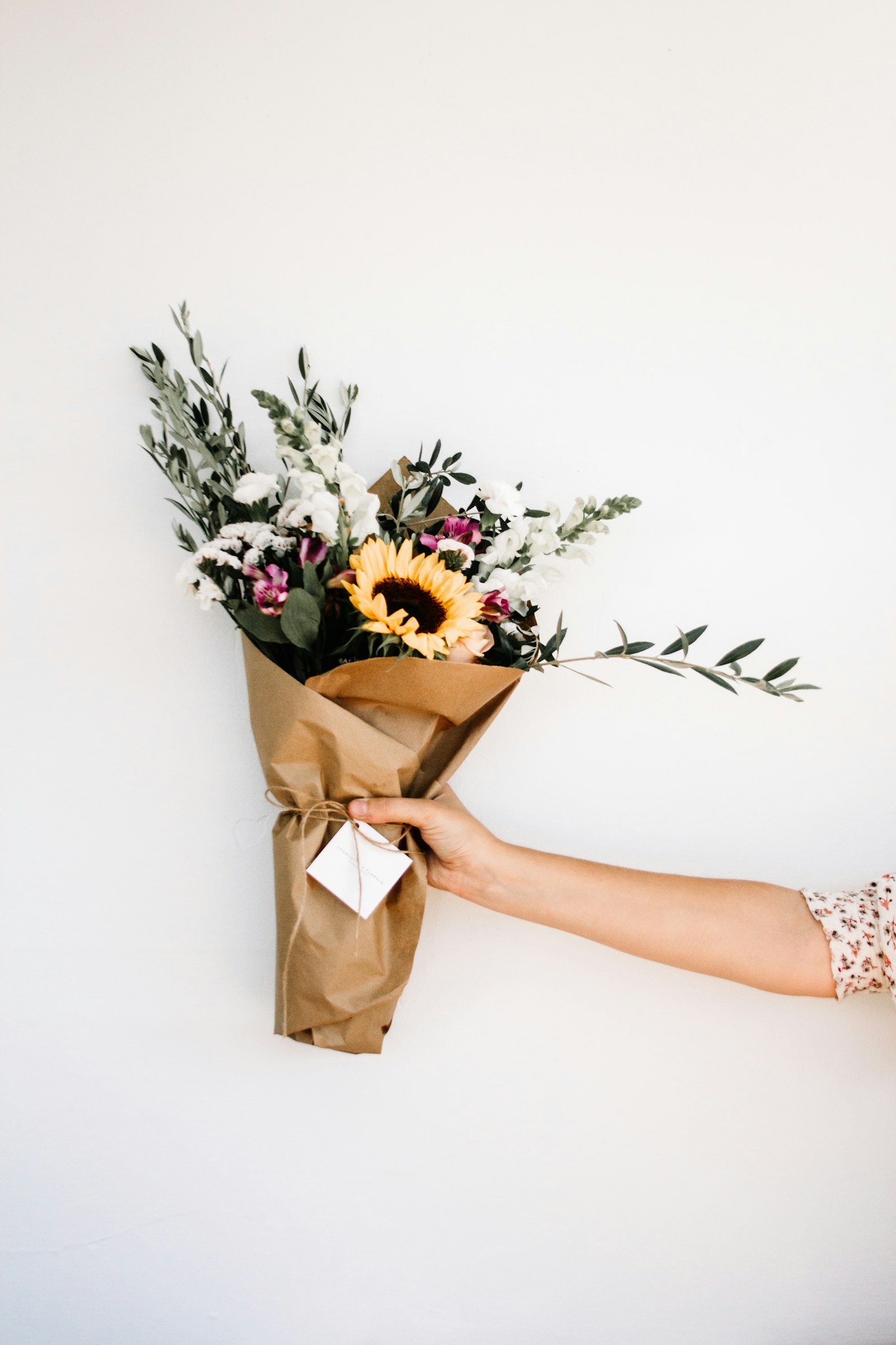 A hand holding a kraft-paper wrapped bouquet with a gift tag