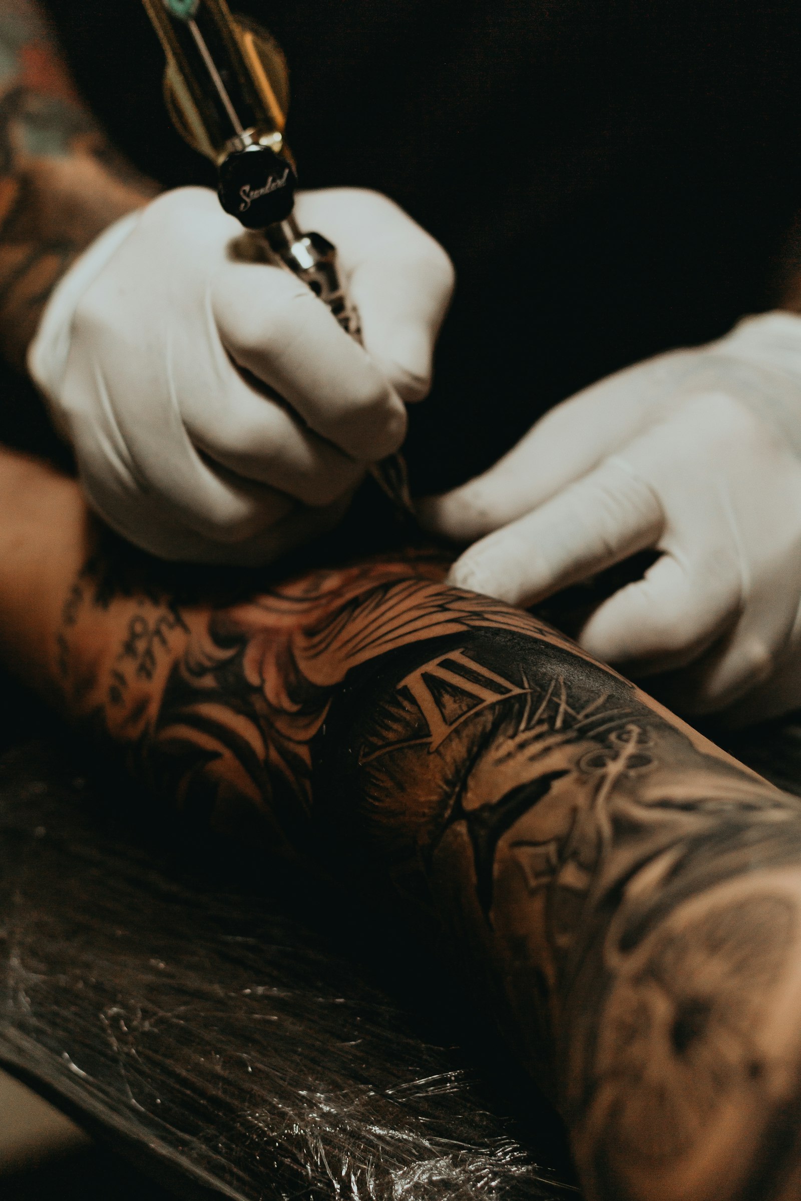 An artist in white gloves working over a heavily inked sleeve