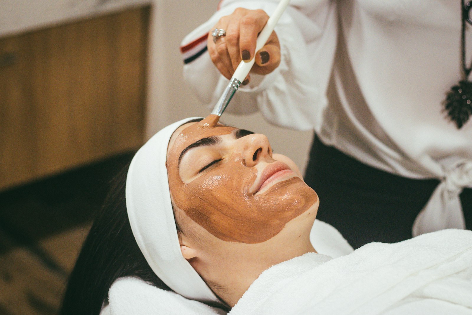 A therapist brushing a clay mask onto a reclined client's face
