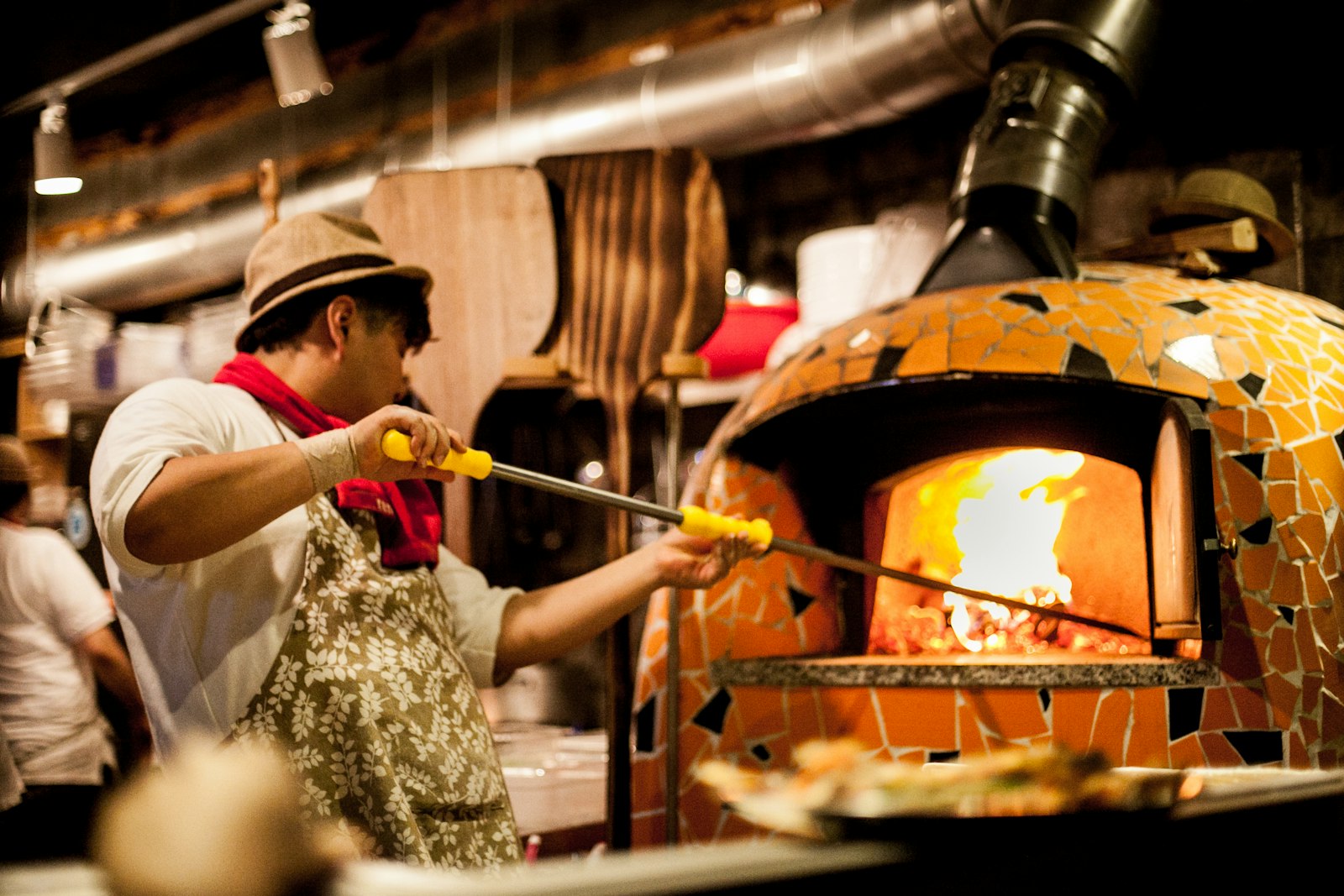 A pizzaiolo working a peel at a tiled wood-fired oven