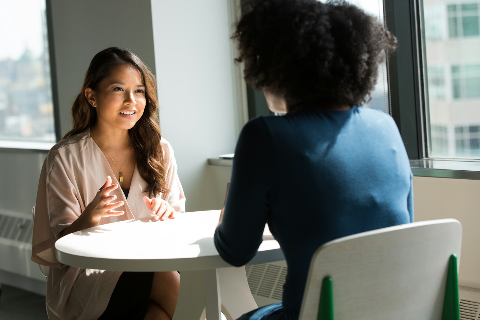 A coach explaining something with her hands to a client seated opposite her at a small table