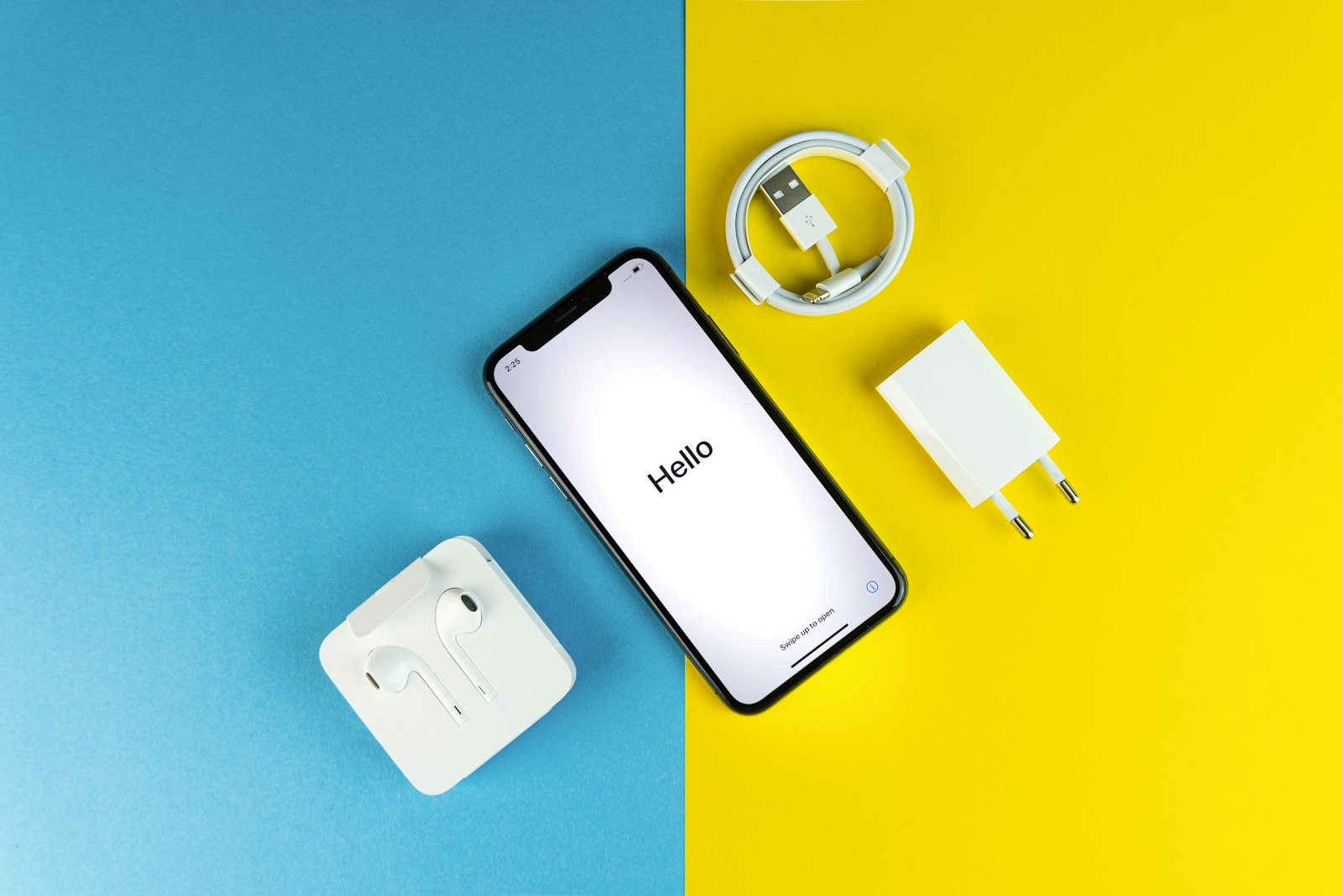 A phone with charger, cable and earbuds on a blue and yellow background