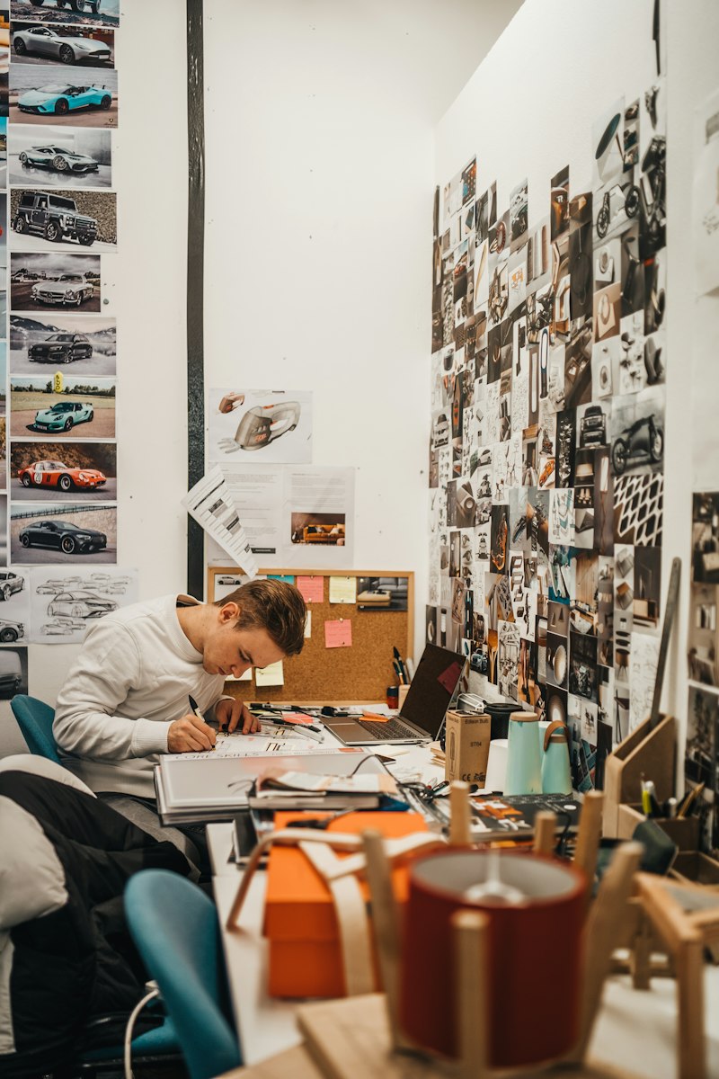 A designer drawing at a desk under a wall of pinned references