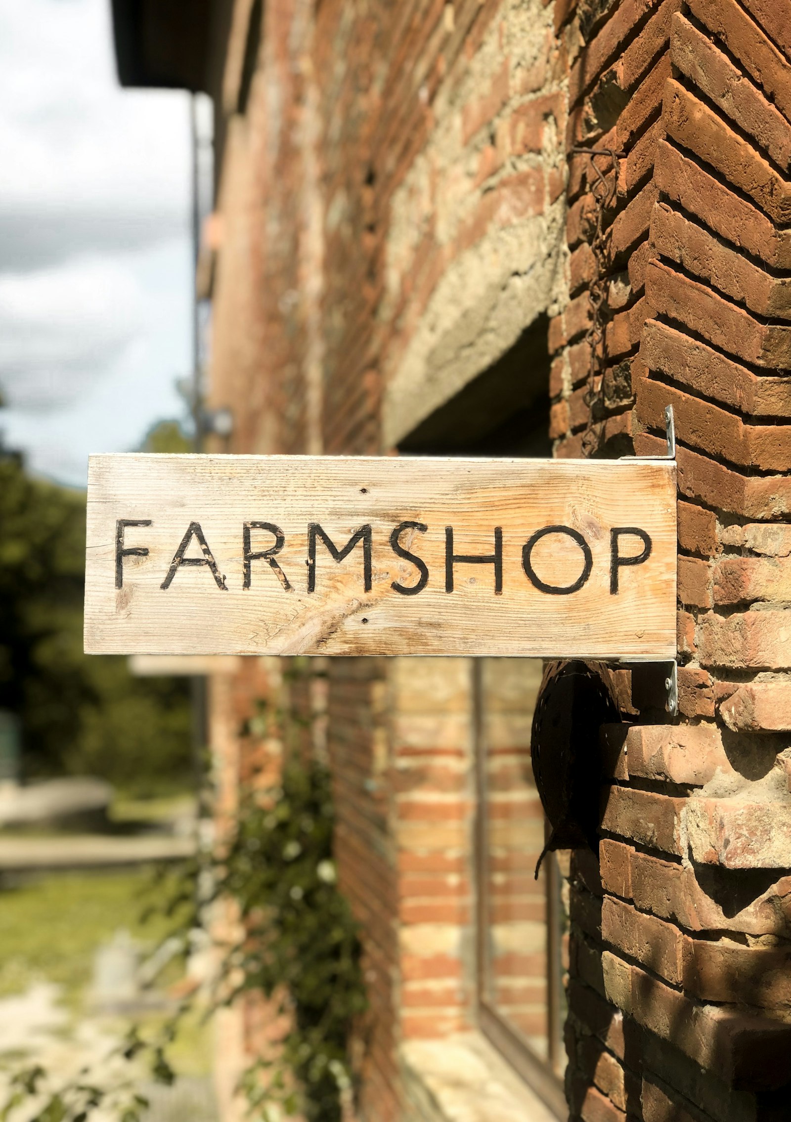 A hand-lettered wooden farm shop sign on an old brick barn wall