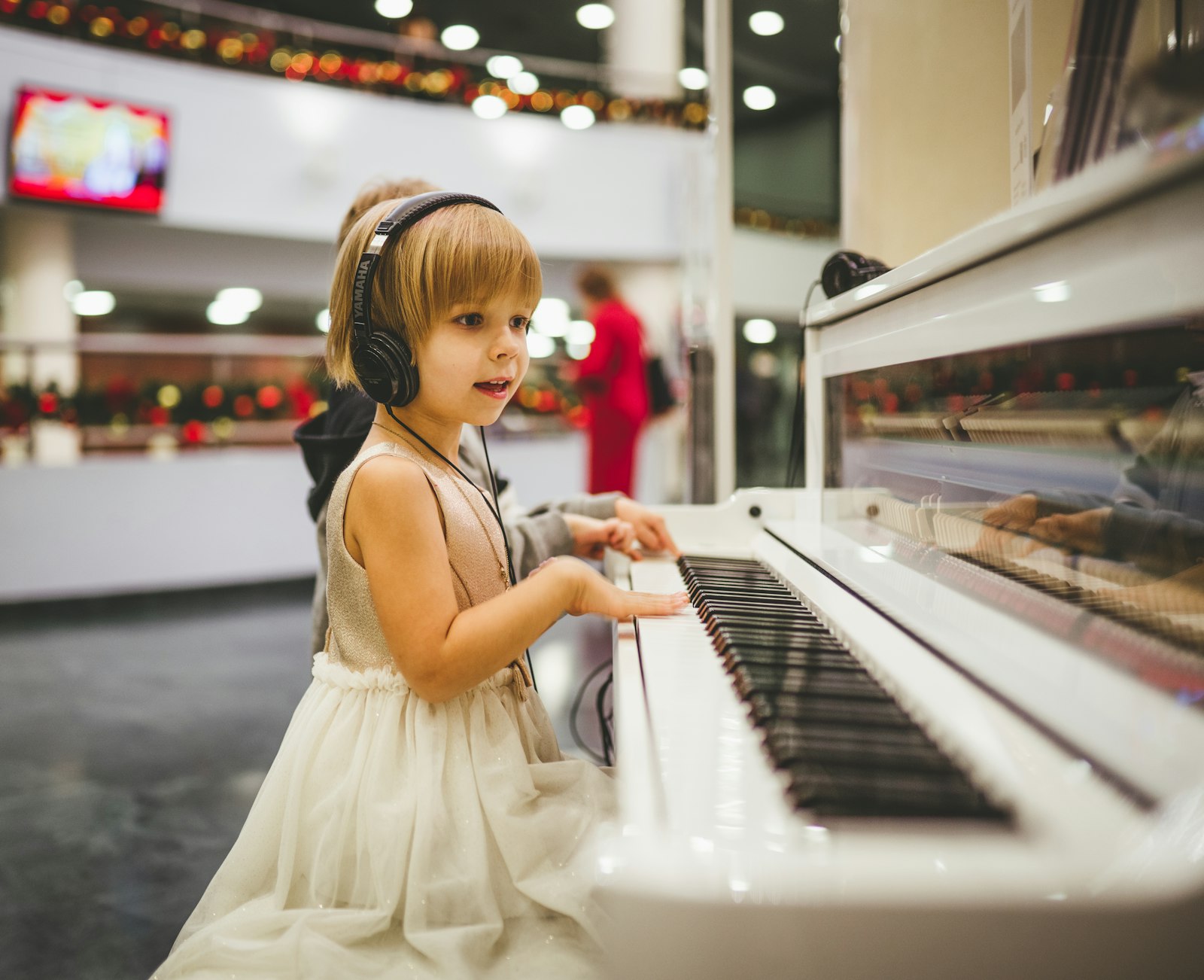 A small girl in headphones at a white piano