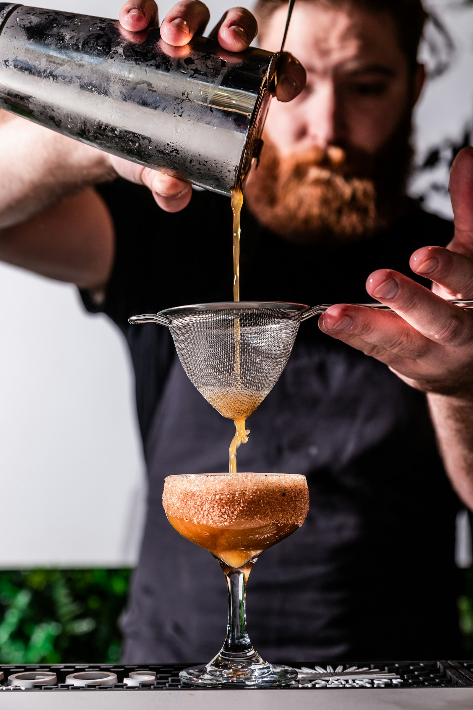 A bartender fine-straining a cocktail into a coupe