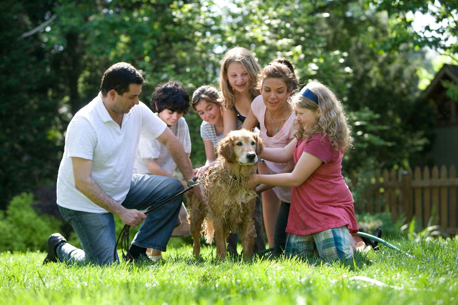 A family gathered round a golden retriever in a sunny garden