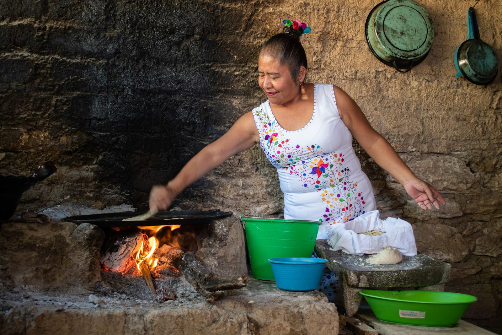A woman cooking tortillas on a comal over a wood fire
