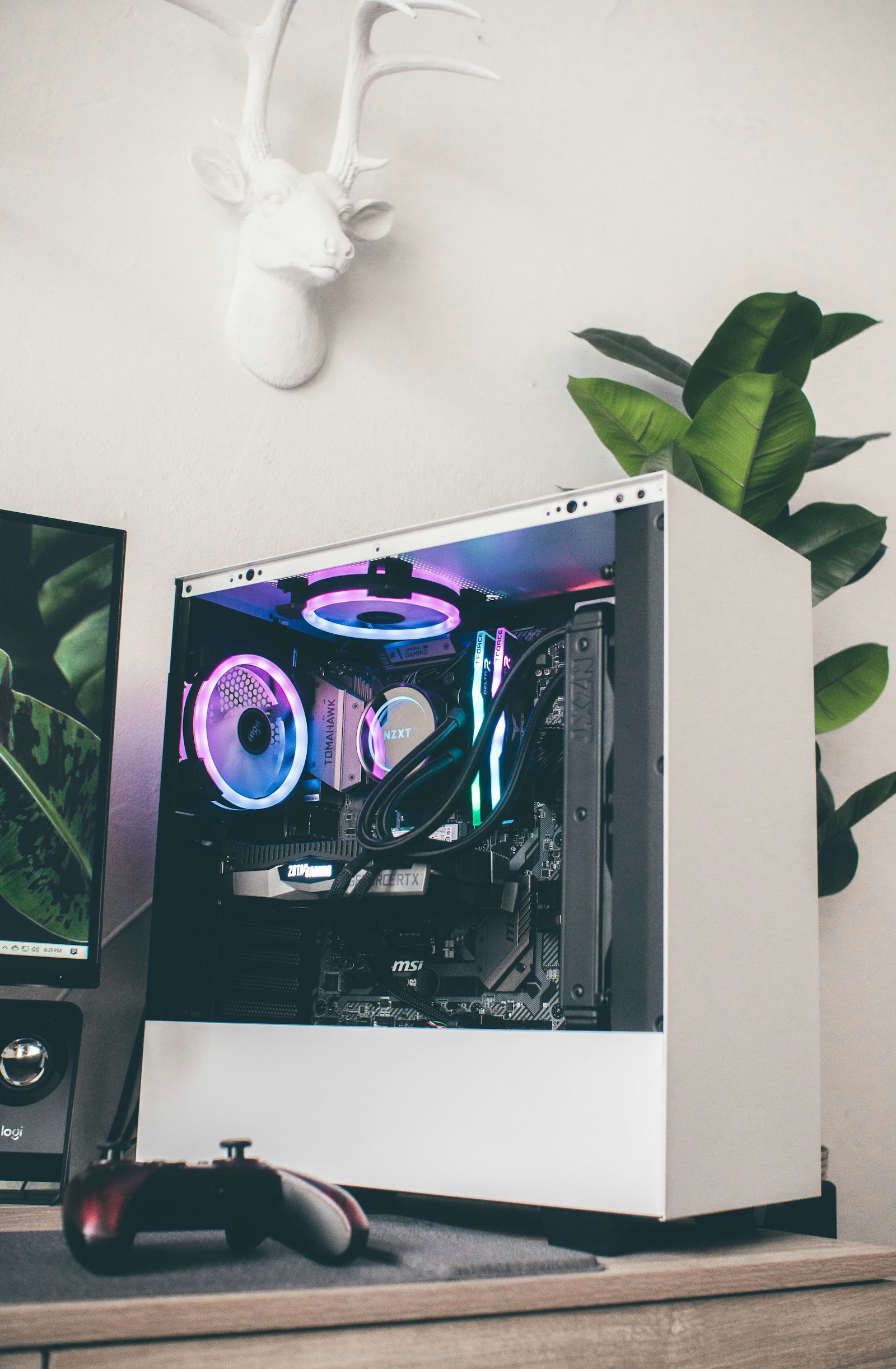 A white custom PC with fans on a desk beside a plant
