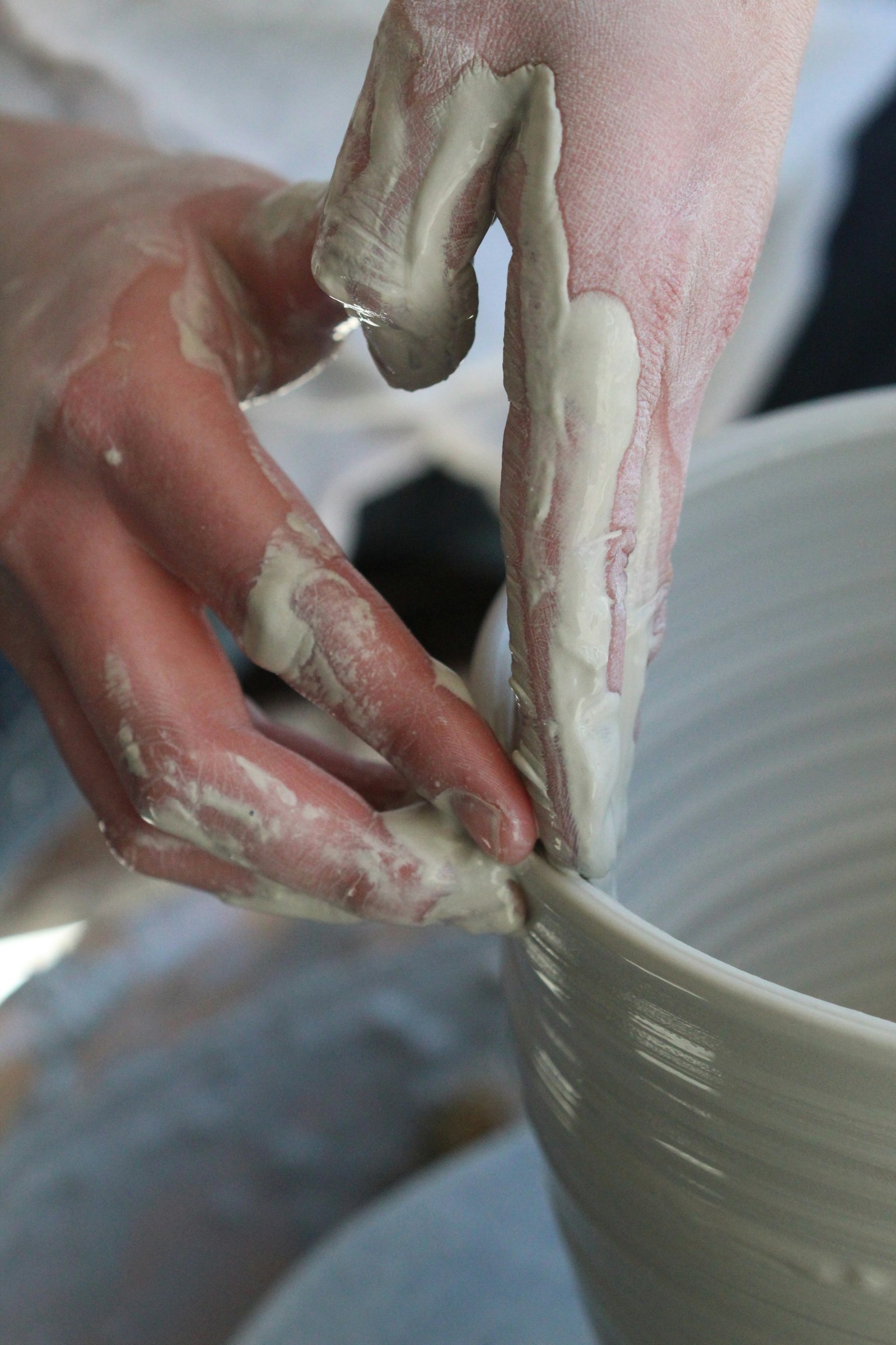Hands trimming the rim of a bowl on the wheel