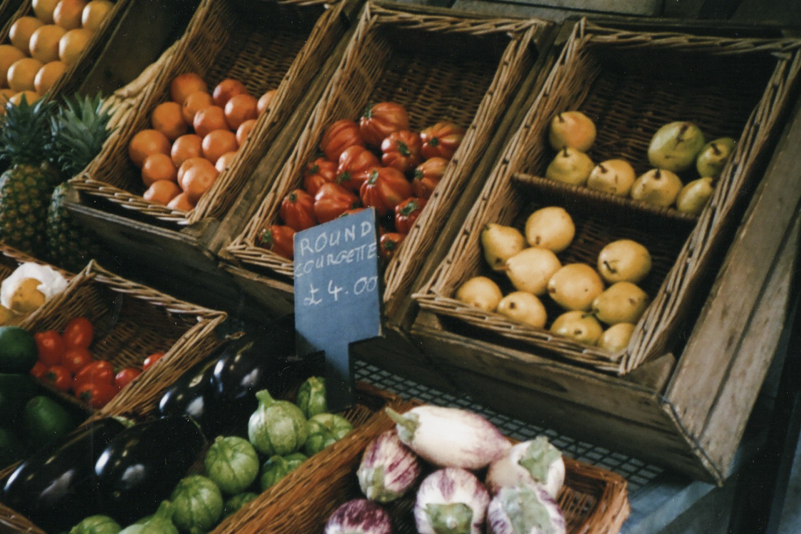 Baskets of tomatoes, oranges and pears with a chalkboard price card