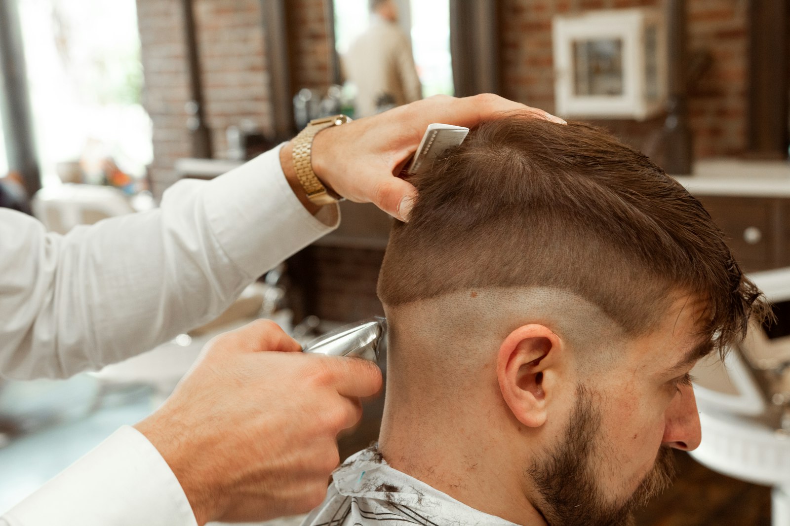 A barber shaping a skin fade with clippers and a comb