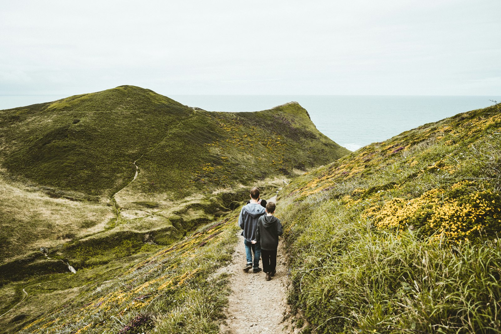 Two walkers on a coastal path through green hills