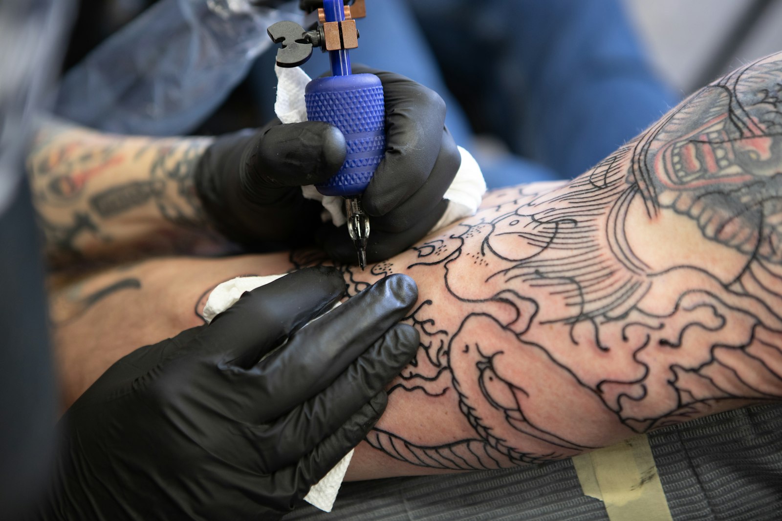 Gloved hands outlining a dragon design on a client's arm