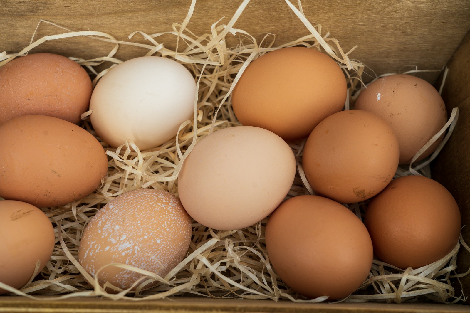 Brown and white eggs in straw in a wooden box