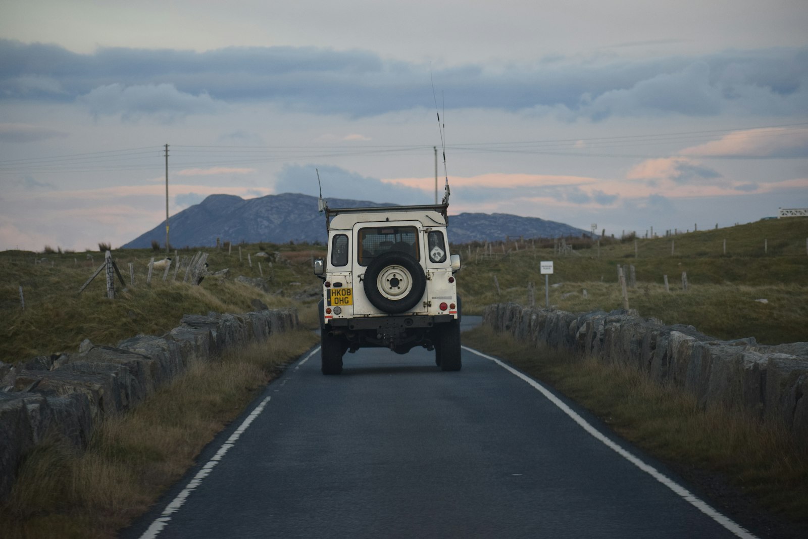 A white Defender from behind on a country road between stone walls
