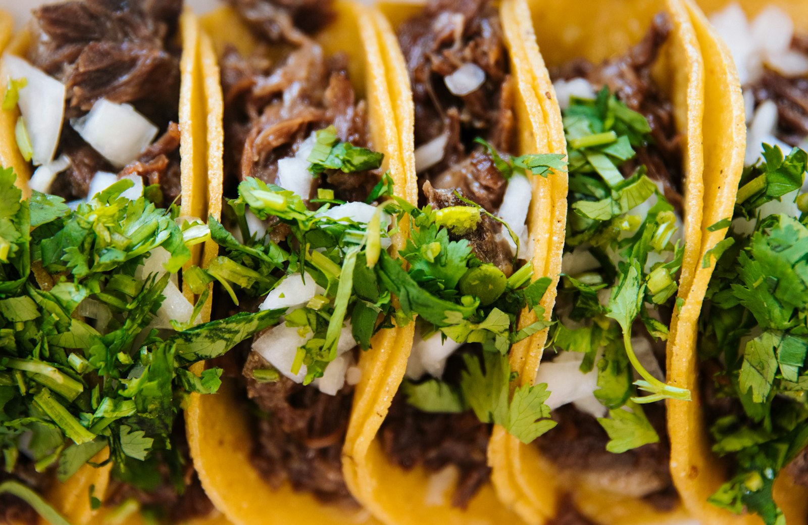 A row of beef tacos with onion and coriander