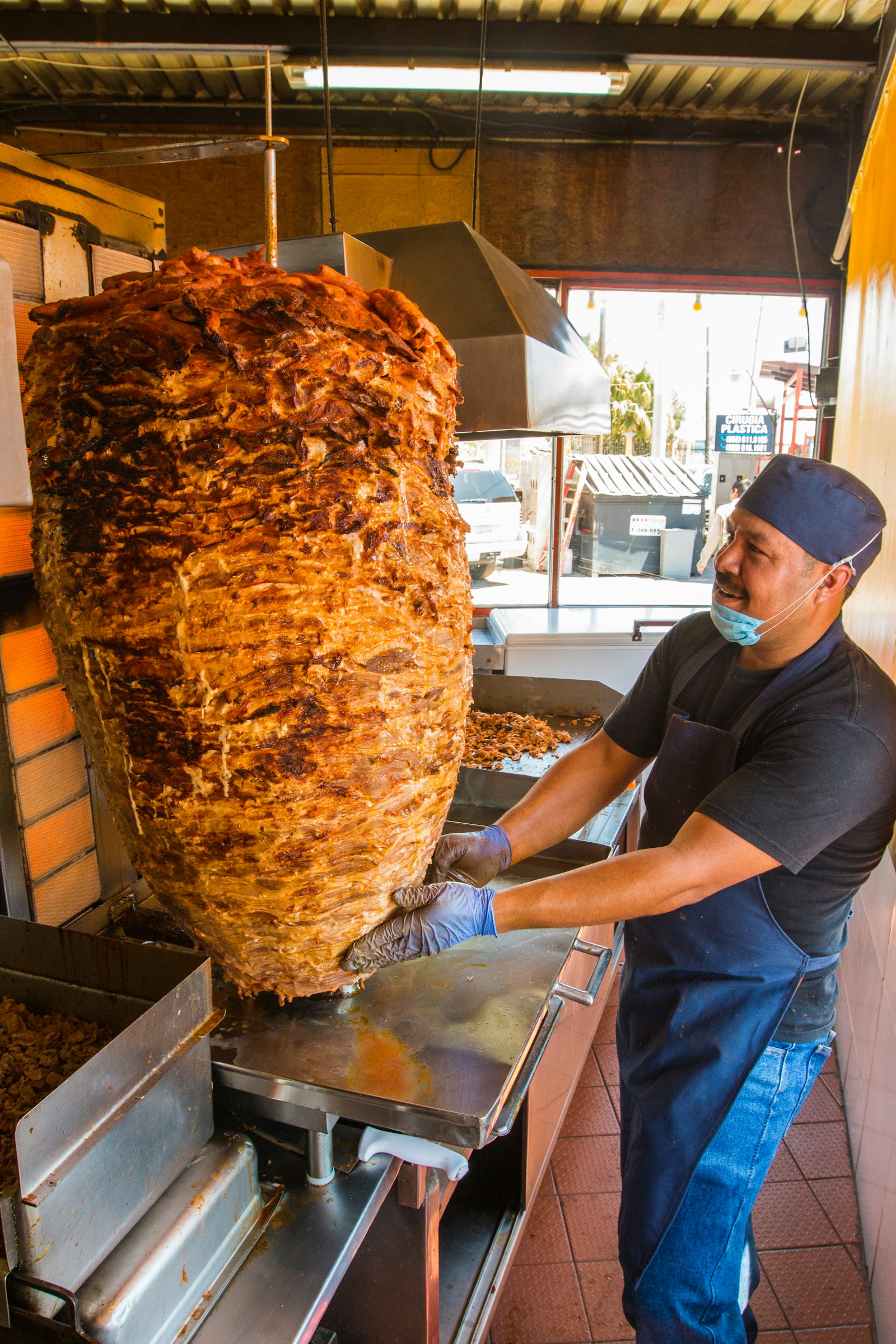 A man at a large al pastor trompo inside a taqueria