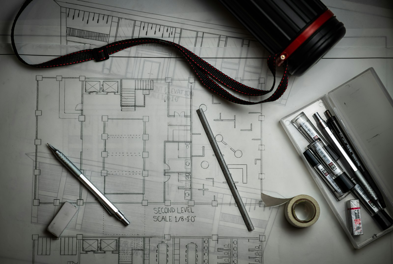 Plan drawings on a desk with pencils, a rule and a drawing tube