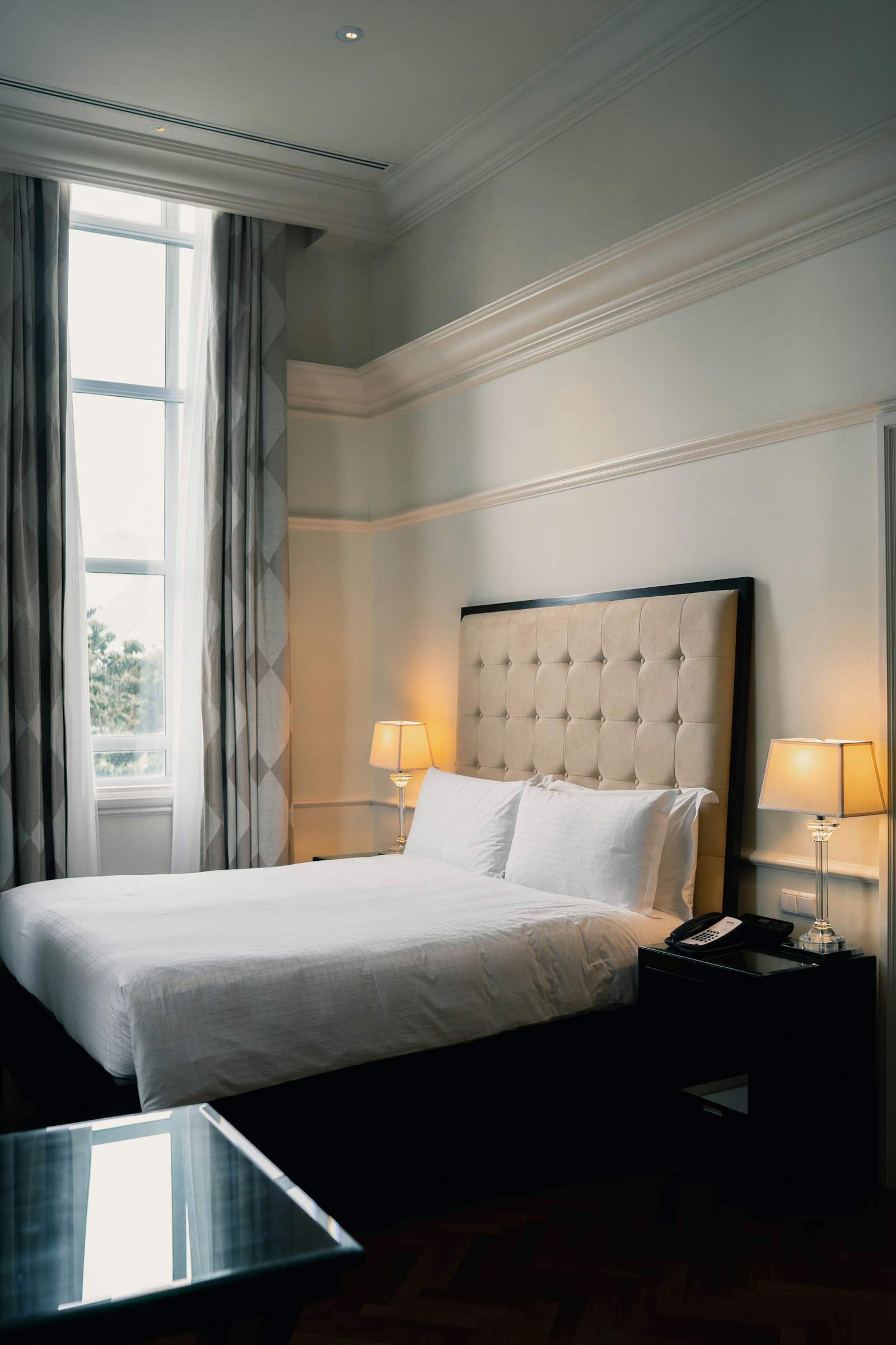 A high-ceilinged bedroom with a tall window and white linen