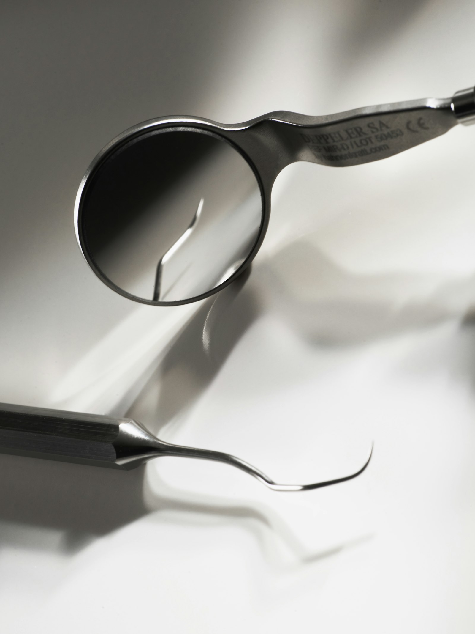 A dental mirror and explorer laid on a white surface