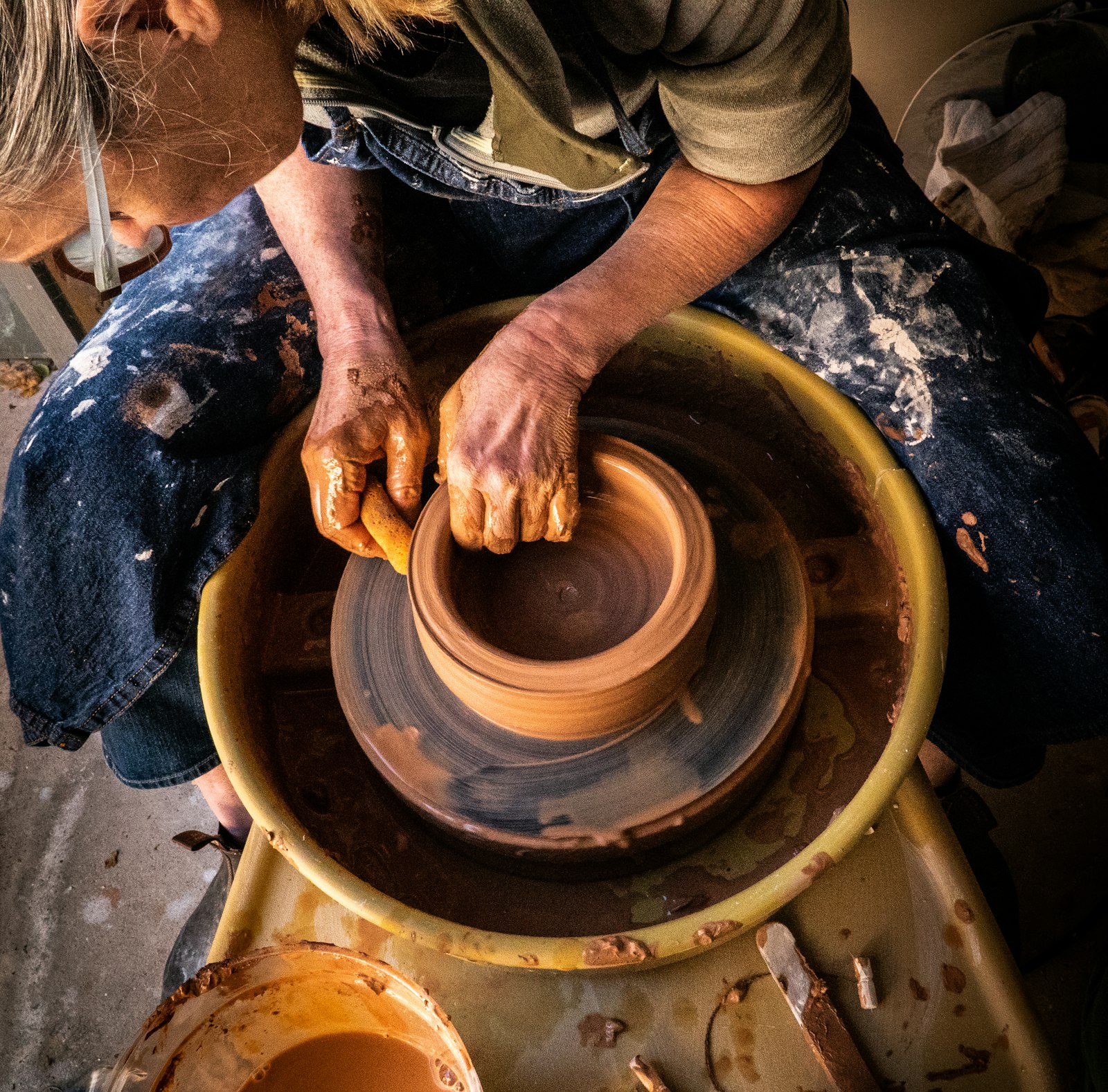A potter in jeans and a striped shirt centring clay
