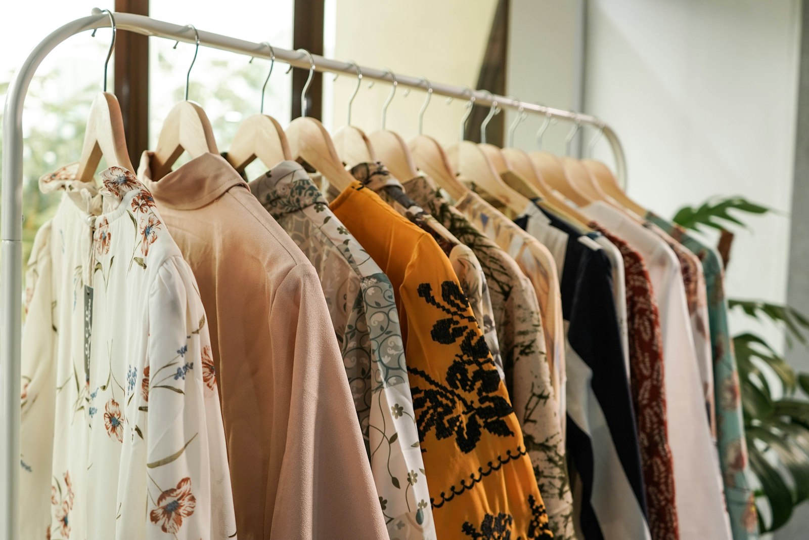 Patterned blouses on wooden hangers by a window