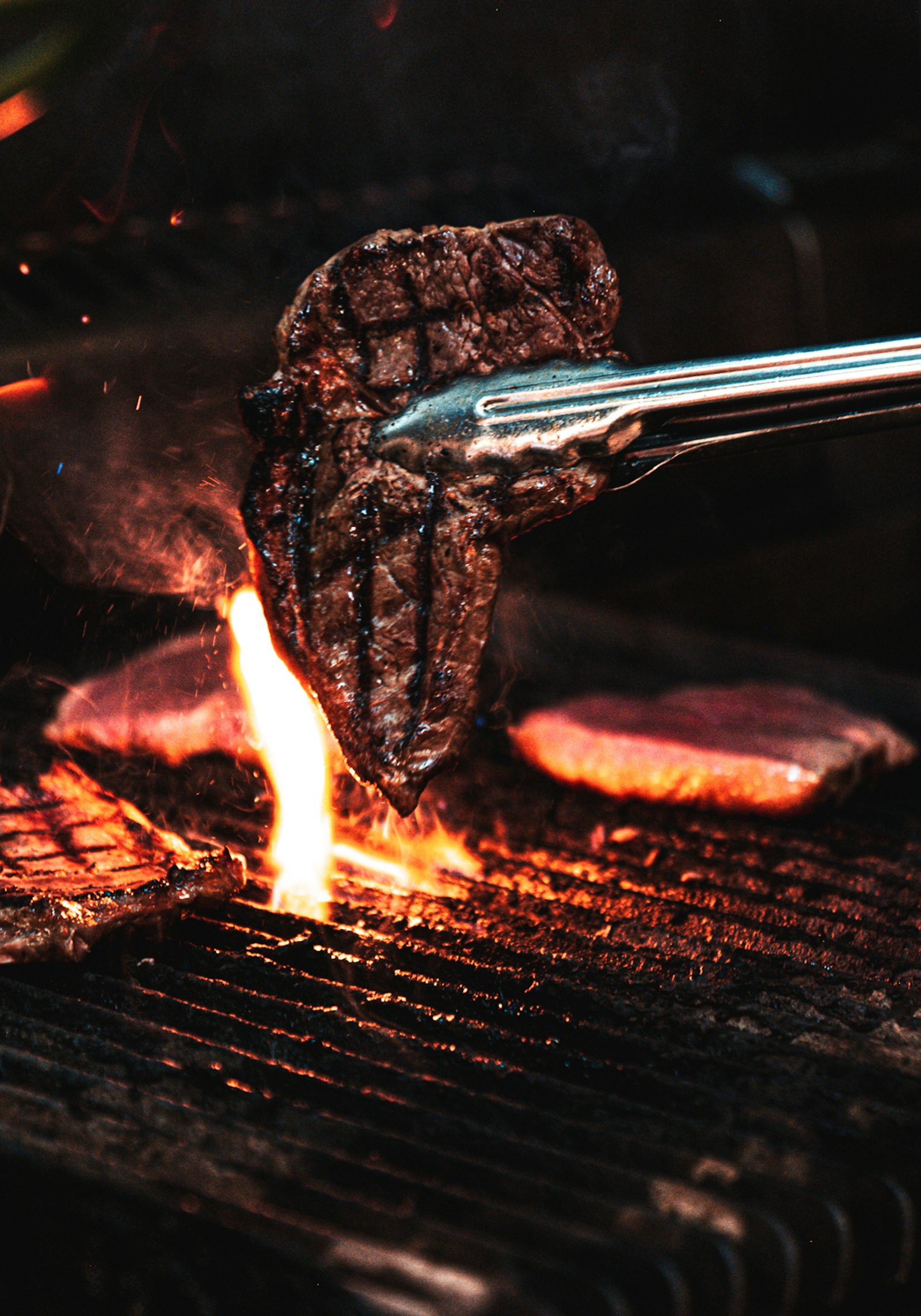Tongs lifting a steak over a charcoal grill